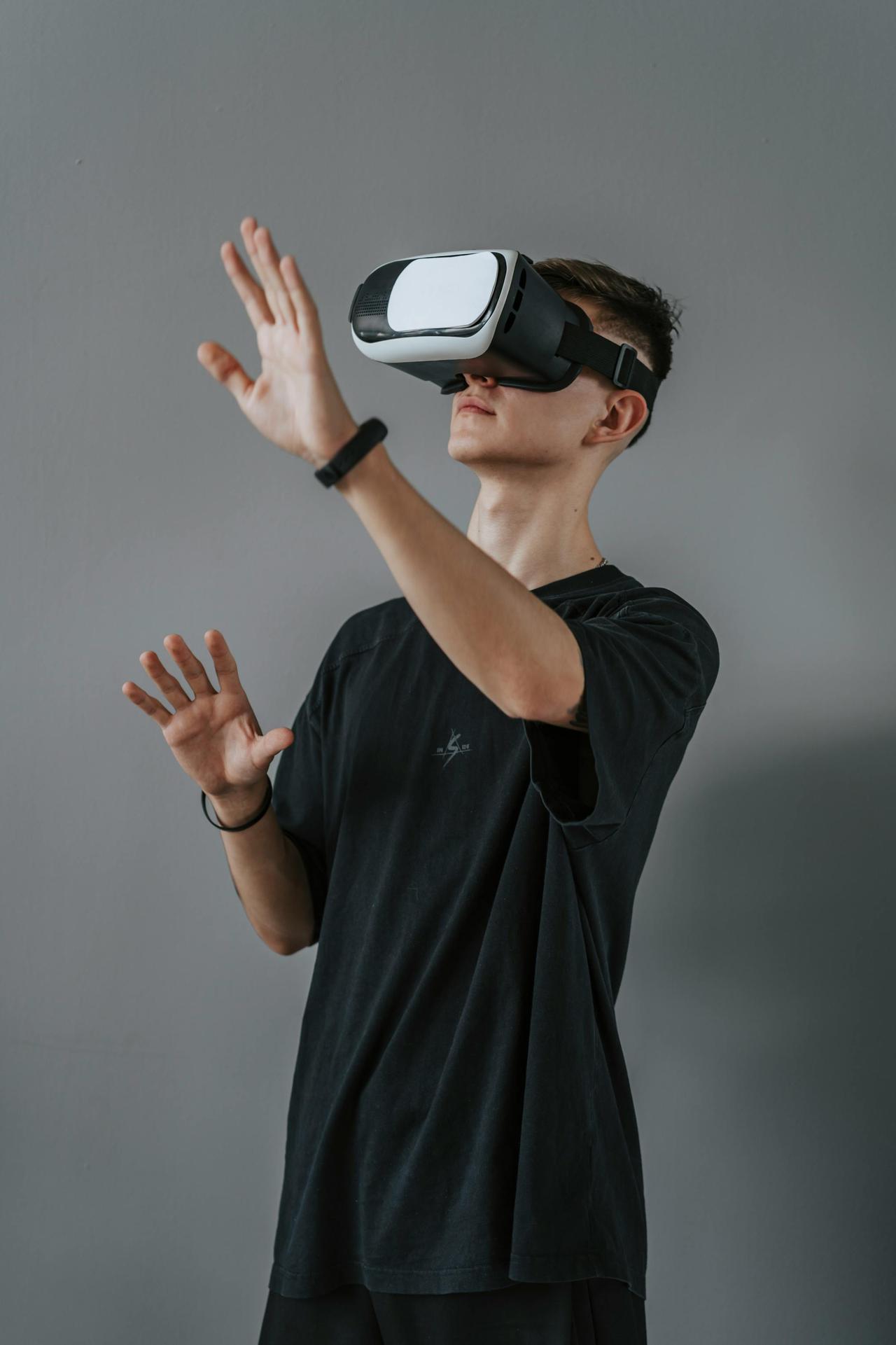 Young man in black shirt enjoying a virtual reality experience using a VR headset against a gray wall.